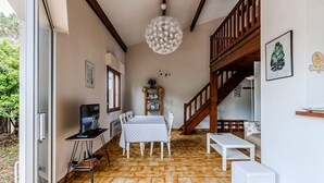A room with a dining table, chairs, a TV, a ceiling light, a staircase, and a bookshelf. - Charming 4-Person Home, Quiet Area Near Beaches, Biscarrosse (Biscarrosse Plage)