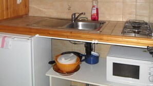 Pieni, käytännöllinen keittiö, jossa on puukehikoiset kaapit, pesuallas, liesi ja mikroaaltouuni.