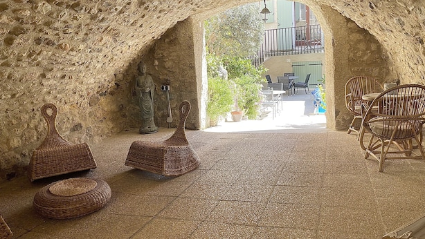 A stone-walled interior with a statue, wicker furniture, and a view to an outdoor balcony. - Gite l'occitan 5 people (autignac)