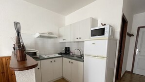 A compact kitchen with white cabinets, a microwave, a stove, and a sink. - Gite l'occitan 5 people (autignac)