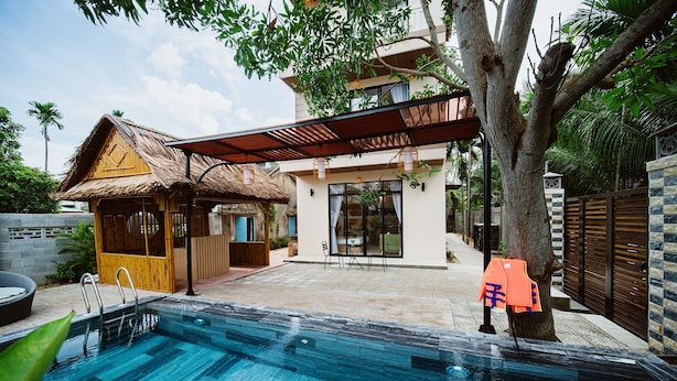 A swimming pool with a wooden deck area, a thatched-roof hut, and a modern house with a covered patio. - BB's Cozy House & Apartment (Da Nang)