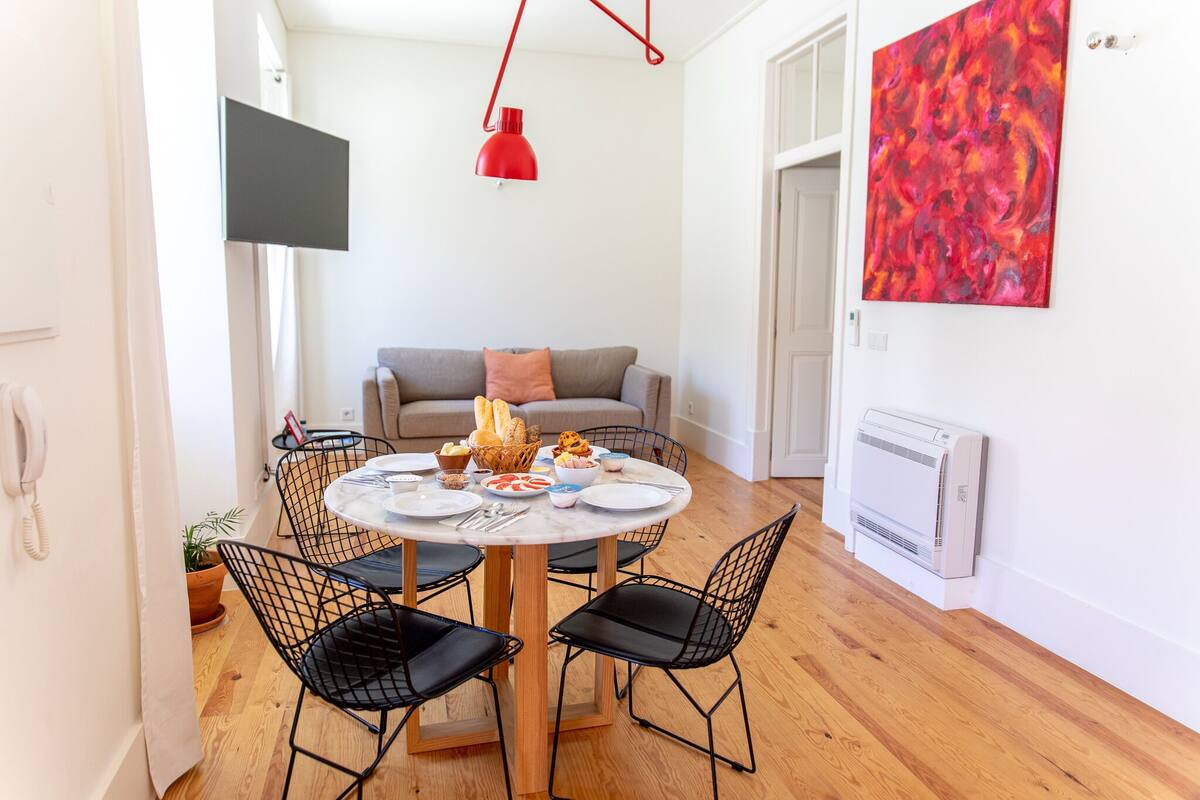 A dining area with a round table, black wireframe chairs, and a red pendant light.