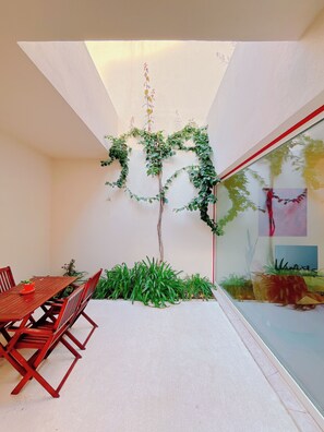A room with a dining table, chairs, a small plant, and a glass partition with a view. - Casa René, Lisbon's Hidden Gem (Almada)