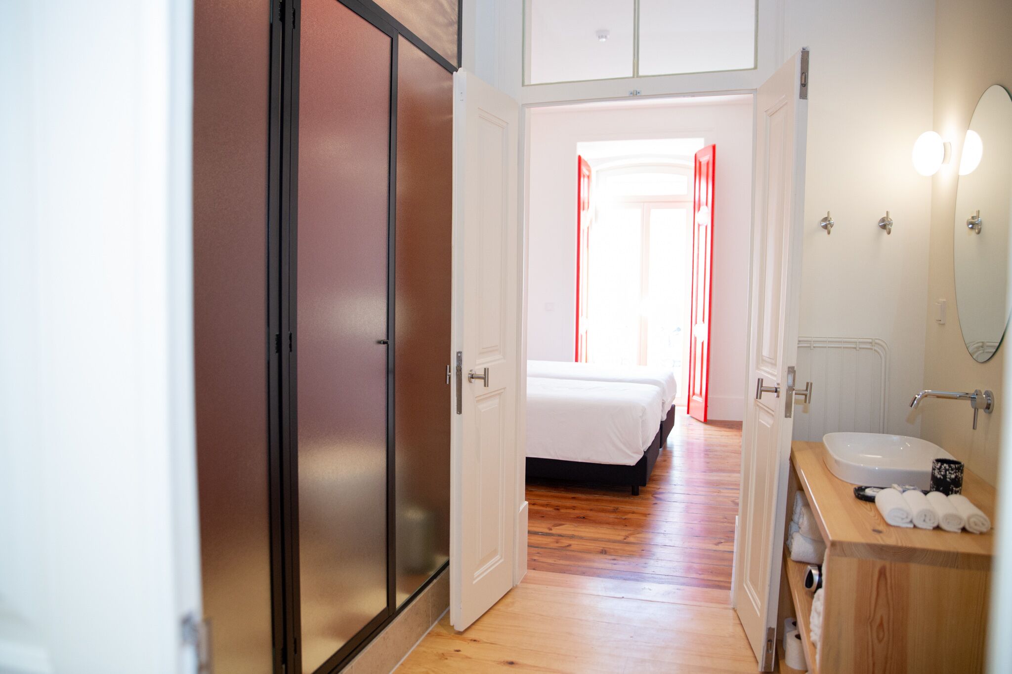 Ein Hotelzimmer mit Holzboden, einem Bett, einem Badezimmer mit Waschbecken und Spiegel sowie einem Kleiderschrank.