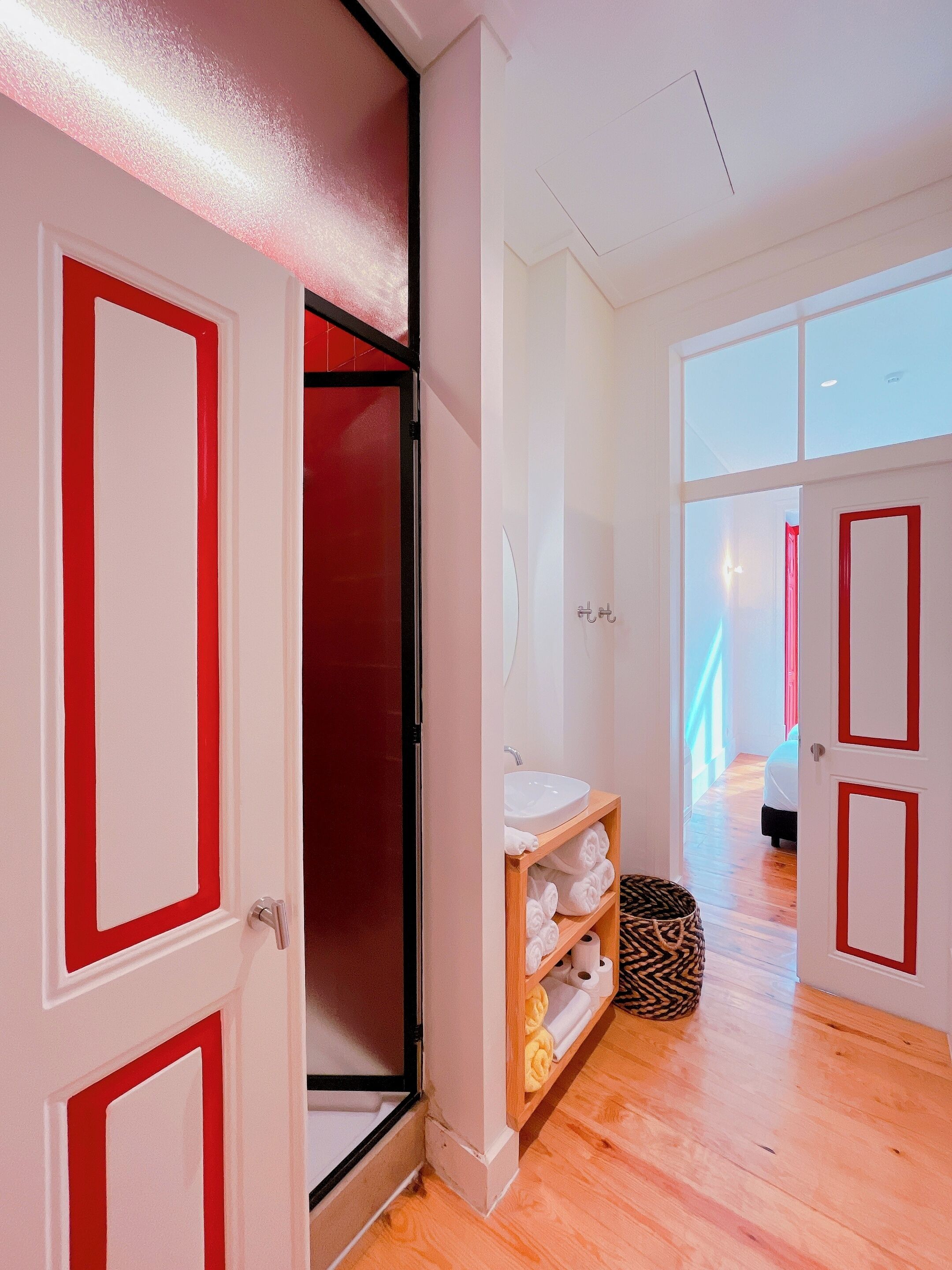 Una porta oberta que dona a un bany amb un lavabo, penjador de tovalloles i paper higiènic.