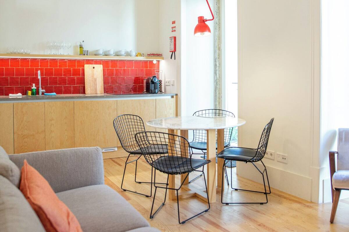 A modern kitchen with red tiles, a wooden countertop, and a dining area with a round table and wire chairs.