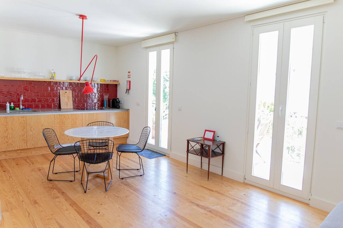 A modern kitchen with a round dining table and chairs, a red pendant light, and a wooden countertop.