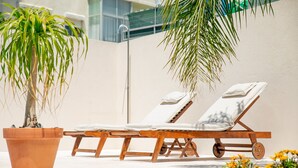 Zona de piscina con dos sillas reclinables de madera y una planta en maceta.