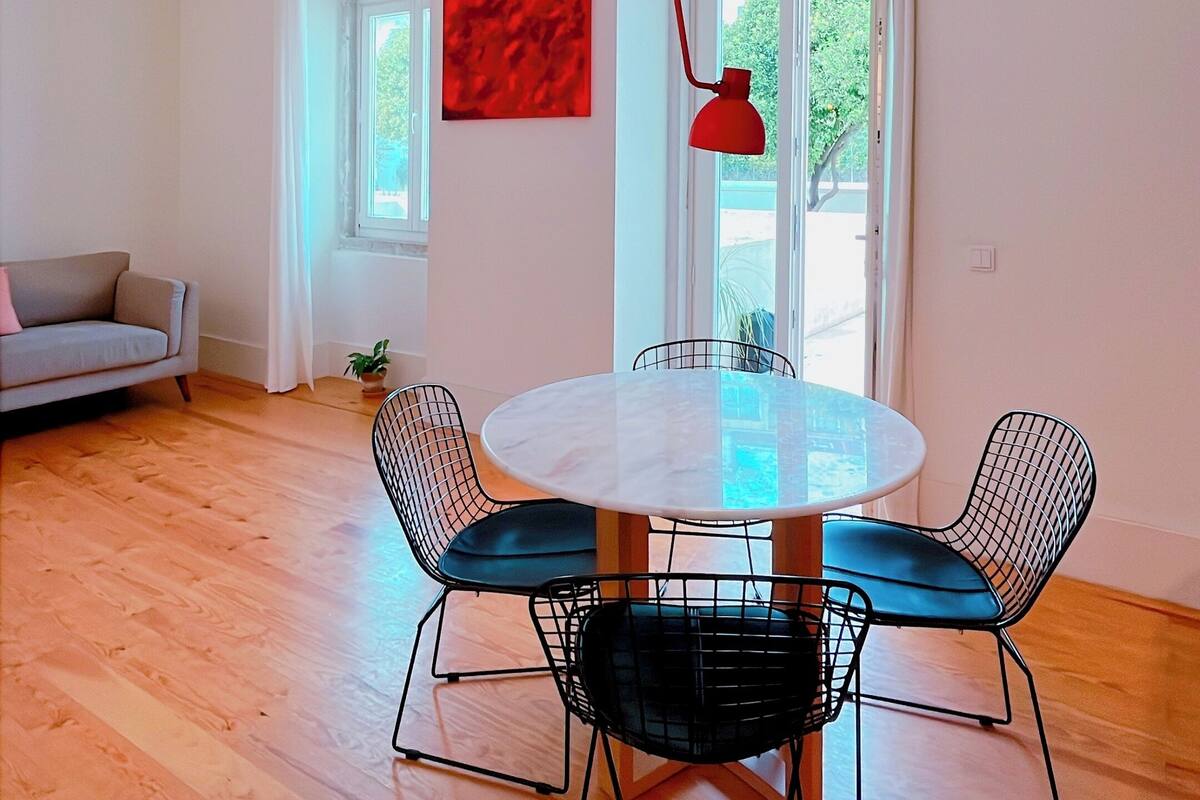 A modern dining area with a round table, black wire chairs, and a red pendant light.