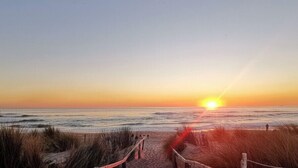 Un sendero de madera que lleva a la playa con un atardecer de fondo.