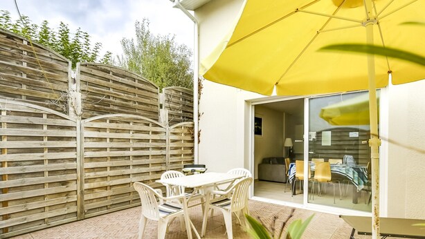 Een terras met een tafel en stoelen, een gele parasol en een houten omheining.