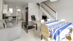 Een moderne woonkamer met een bank, een eettafel met stoelen, een trap en een keuken op de achtergrond.