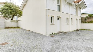 Een huis met twee verdiepingen, met een witte gevel en een pannendak, en een oprit van grind.