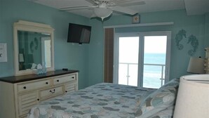 Une chambre à coucher comprenant un lit, une commode, un téléviseur et une vue sur l’océan, accessible par une porte coulissante.