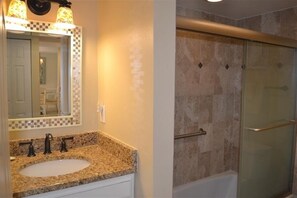 Une salle de bain dotée d’un lavabo avec un plan de travail en granit, d’un miroir bordé de mosaïques et d’une douche avec une porte en verre.