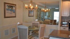 A dining area with a glass table, wicker chairs, and a chandelier. - Beachcomber unit 404 (Longboat Key)