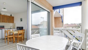 A balcony with a white table and chairs, a sliding glass door, and a view of buildings.