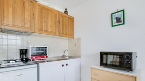 A compact kitchen with wooden cabinets, a white refrigerator, a toaster, a sink, and a microwave.