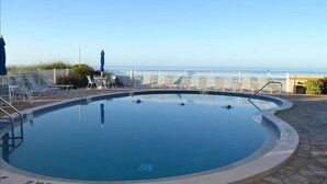 Ein Schwimmbecken mit Blick auf den Ozean, umgeben von Liegestühlen und Sonnenschirmen.