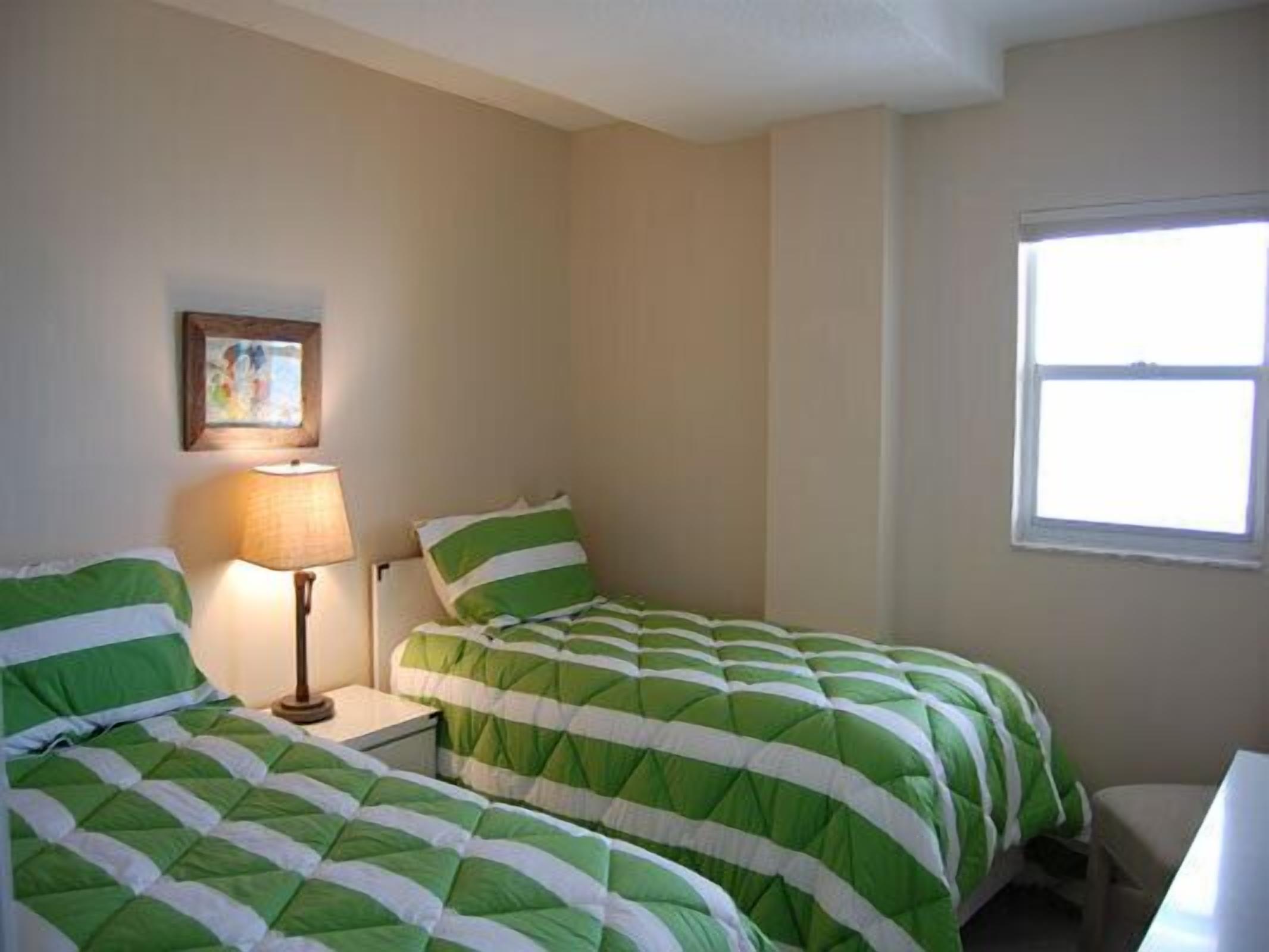 A room with two beds, a nightstand, a lamp, a window, and a painting on the wall.