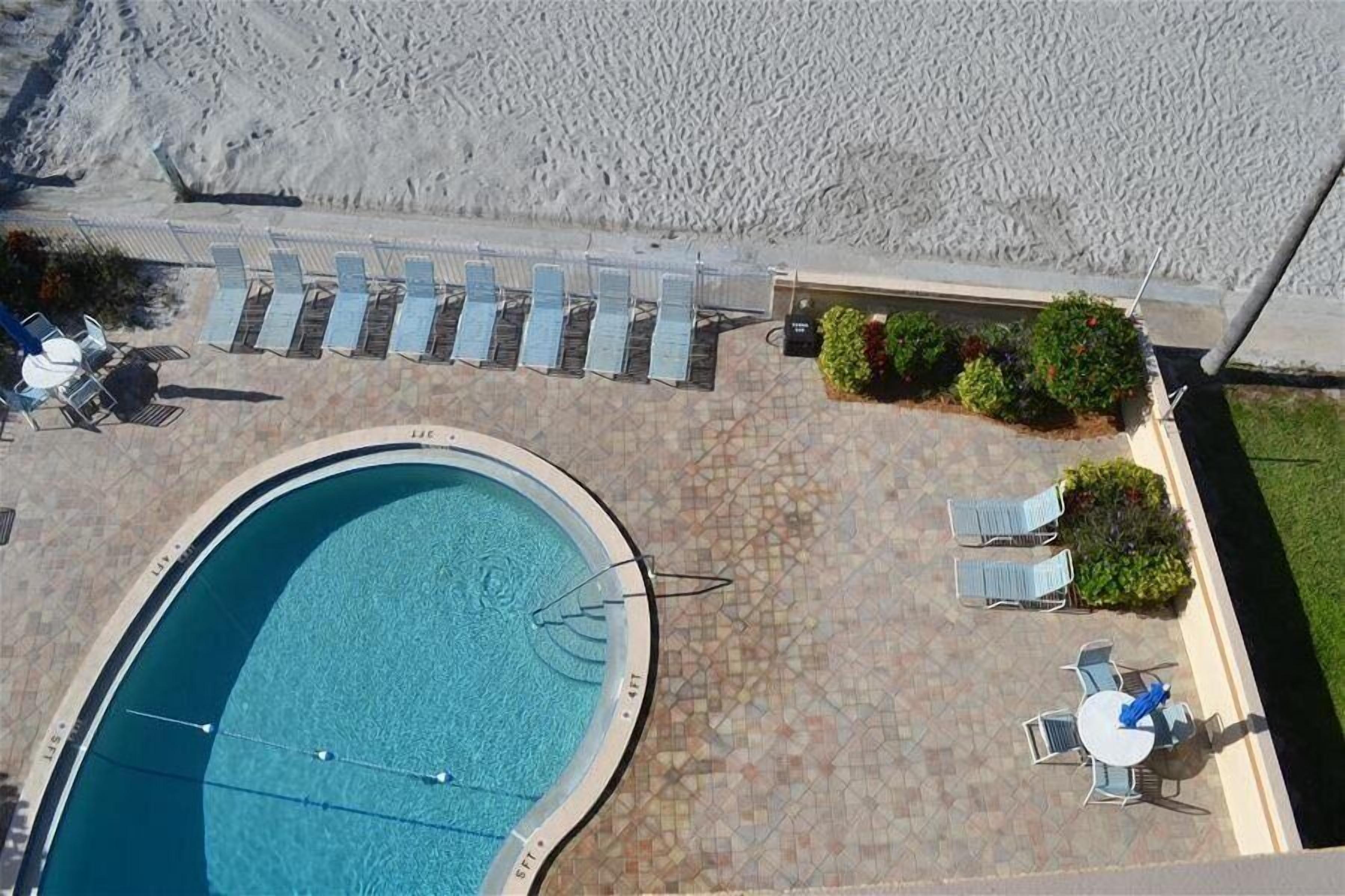 An outdoor swimming pool with lounge chairs and a table, surrounded by a tiled patio area.