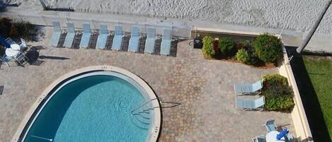 An outdoor swimming pool with lounge chairs and a table, surrounded by a tiled patio area.