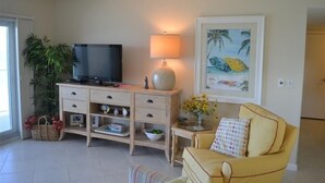 Ein Wohnzimmer mit Fernseher auf einer Holzkommode, einer Lampe, einem Sofa und einem Bild an der Wand.