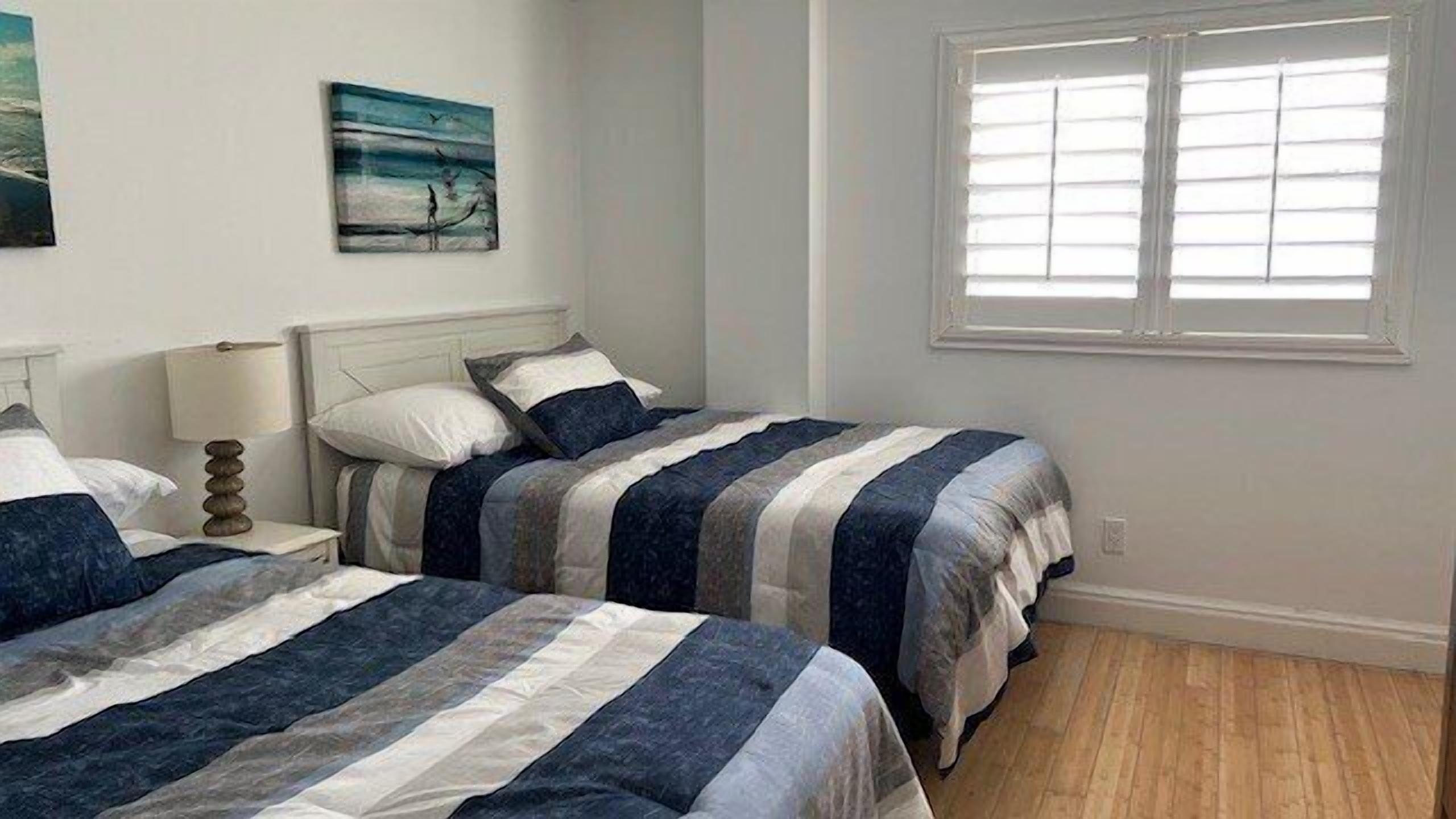 A bedroom with two beds, a nightstand, a lamp, and a window.