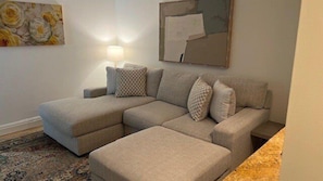 A living room with a sectional sofa, a lamp, and a painting on the wall.