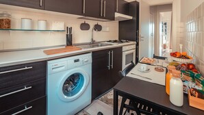Een moderne keuken met donkere kastjes, een Bosch wasmachine, een spoelbak en een ontbijtgedeelte met fruit en een fles melk.