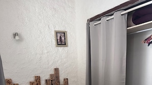 Un lit bien fait, avec une couvre-lit à motifs, une tête de lit en bois et une petite table de chevet surmontée d’une lampe.