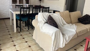Un salon avec un canapé beige, une table à manger avec des chaises, un meuble et un miroir au mur.