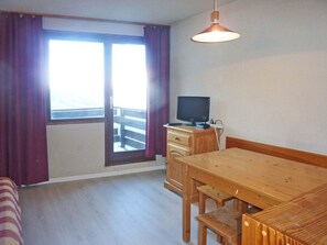 A room with a wooden table, a TV on a wooden cabinet, and a window with curtains.