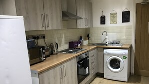 A modern kitchen with wooden cabinets, a built-in oven, a washing machine, and a sink. - Cultural quarter apartments (Leicester)