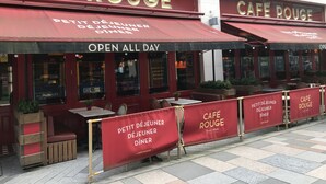 An outdoor seating area of Café Rouge with red awnings and wooden furniture. - Cultural quarter apartments (Leicester)