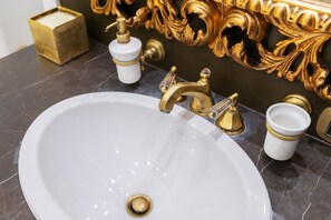 A white sink with gold fixtures, a gold soap dispenser, and a gold candle holder on a marble countertop.
