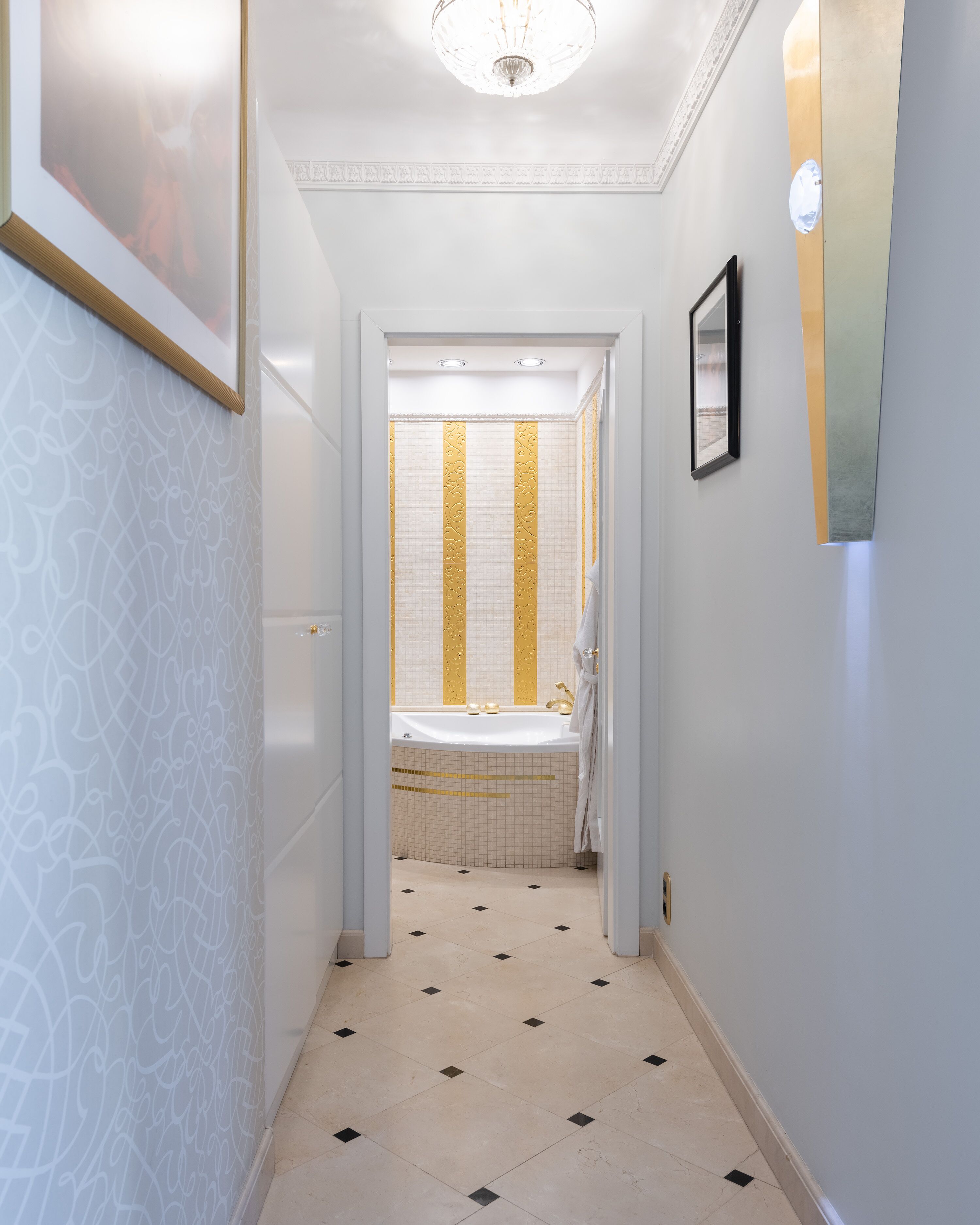 Un pasillo estrecho con paredes estampadas, piso de baldosas y un baño con bañera y ducha.