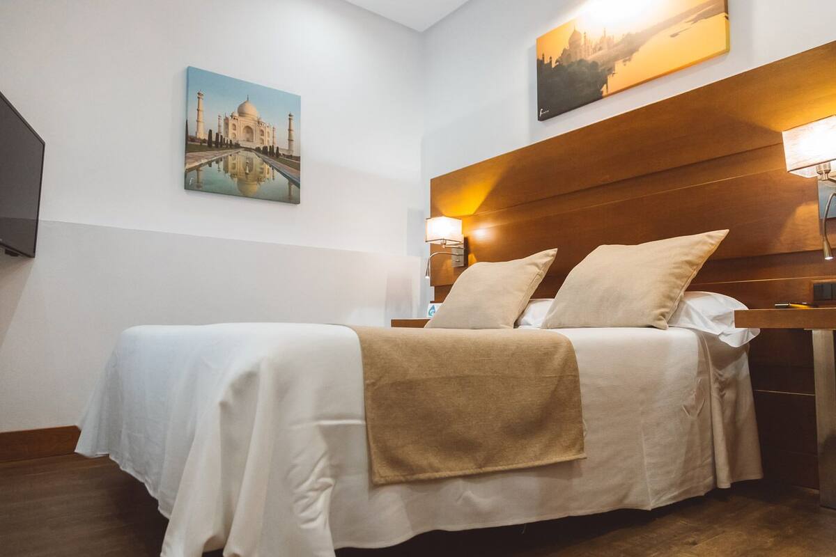 A hotel room with a bed, a nightstand, a lamp, and two paintings on the wall.