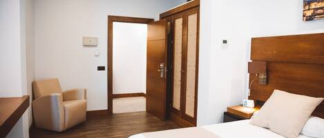 Une chambre d’hôtel avec un lit, une chaise, une armoire en bois et une table de chevet avec une lampe.