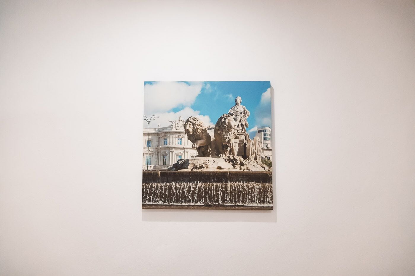 A photograph of a classical sculpture on a pedestal, set against a backdrop of buildings and a clear sky.