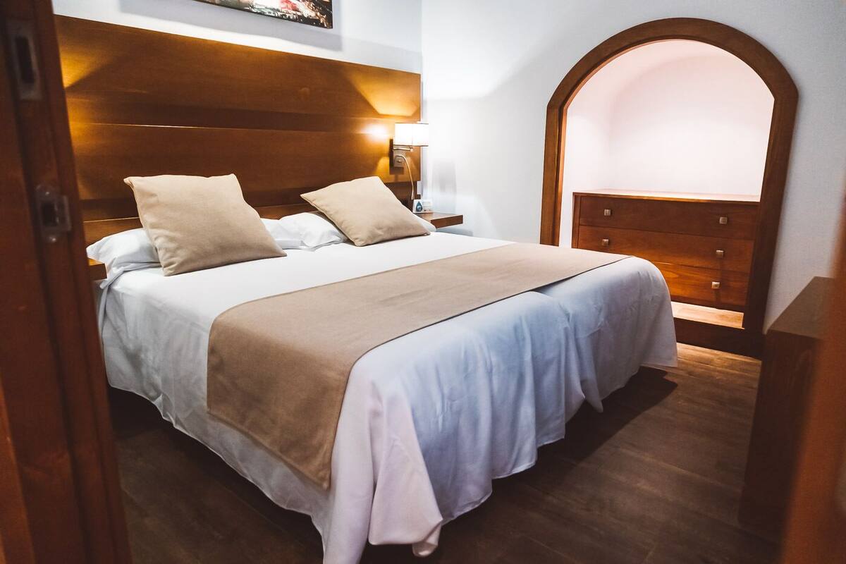 A neatly made bed with a wooden headboard, a bedside table with a lamp, and a wooden arched niche.