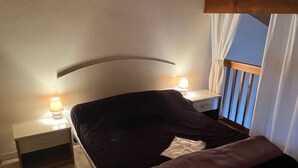 Un lit simple avec une tête de lit, deux tables de chevet avec des lampes, une fenêtre avec des rideaux et un plancher en bois.