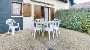Une maison dotée d’un patio comprenant une table et des chaises, une porte en bois et une haie.