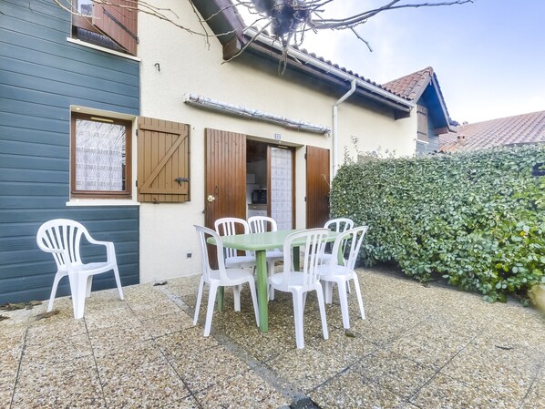 A house with a patio area featuring a table and chairs, a wooden door, and a hedge.