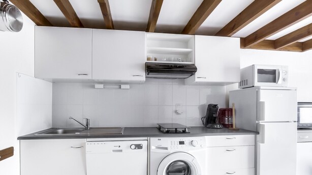 Une cuisine compacte dotée de meubles blancs, d’un lave-vaisselle encastré, d’un lave-linge à chargement frontal, d’un four à micro-ondes et d’une machine à café.