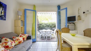 Une pièce avec un canapé gris, une table à manger avec des chaises, un téléviseur et une vue sur l’extérieur.