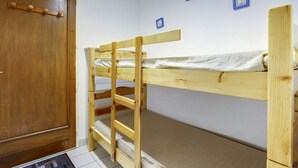 Un lit superposé dans une pièce avec une porte en bois et un sol carrelé.