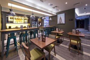A bar area with stools, tables, and a bar counter with bottles. - Premier Inn Liverpool Lime Street (Liverpool)