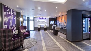 A modern hotel lobby with check-in counters, seating area, and a self-service kiosk. - Premier Inn Liverpool Lime Street (Liverpool)