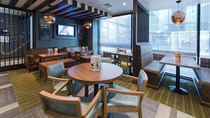 A modern interior with a round wooden table, cushioned seating, and a television mounted on the wall. - Premier Inn Liverpool Lime Street (Liverpool)